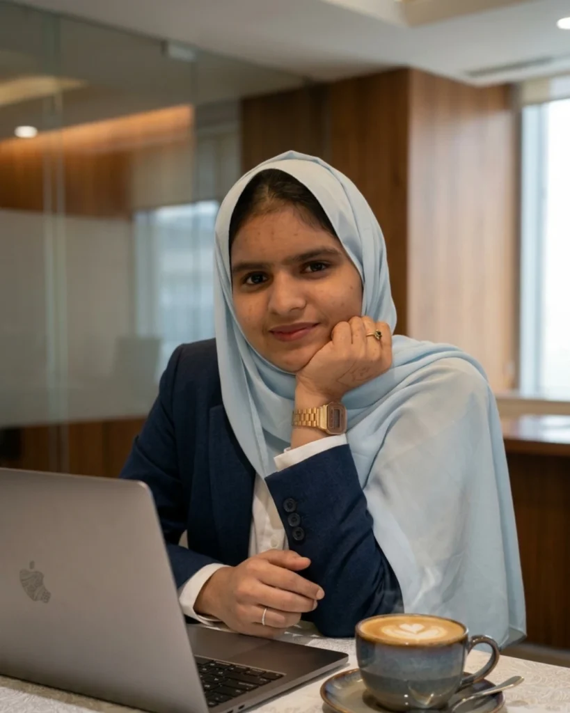 Female freelance digital marketing specialist in Qatar working on a laptop in a modern office setting with a coffee on her side.